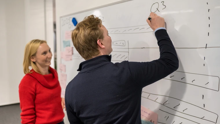 A man and a woman stand in front of a whiteboard and draw up a plan